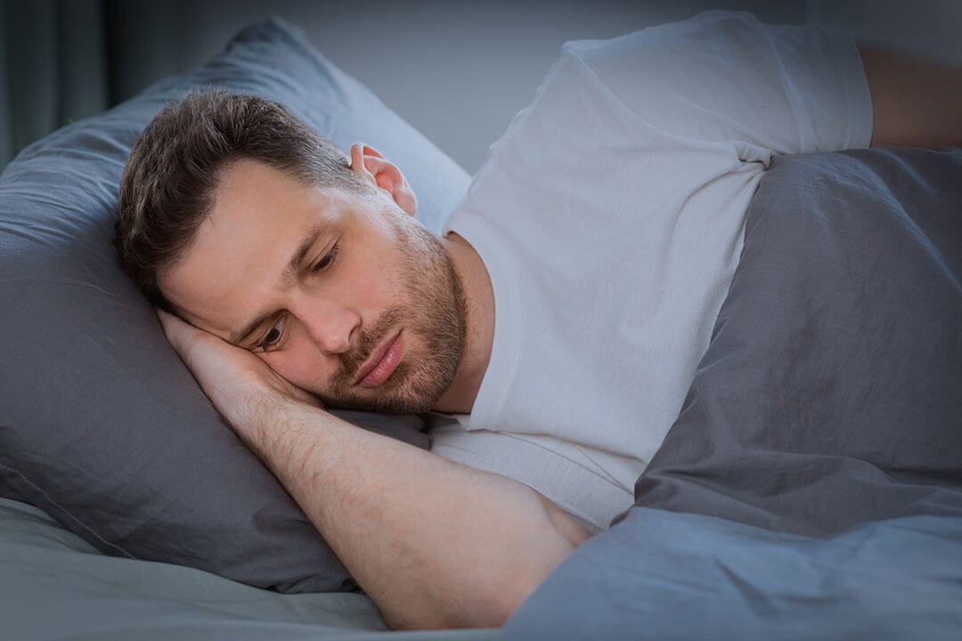 Young man seeks sleep while anxiety keeps him awake in bed at night