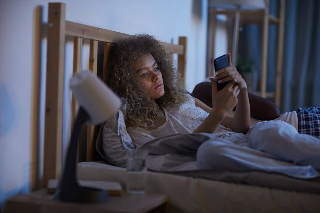 Young woman uses smartphone in bed at night
