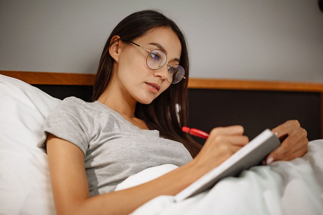 Young woman journaling while laying in bed