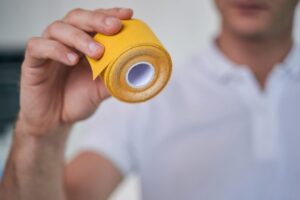 A man's hand holding bright yellow kinesiology tape.