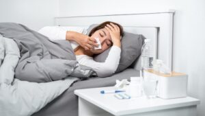 stock photo of a sick woman blowing her nose while lying in bed