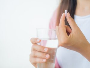 stock photo of a woman holding a pill and a glass of water