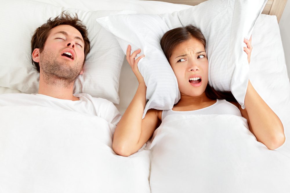 stock image of a woman covering her ears with a pillow because of her partner's snoring